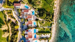 Vista aérea de un complejo turístico costero con varias villas, una piscina y una playa.