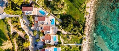 Vista aerea di una località balneare con diverse ville, una piscina e una spiaggia.