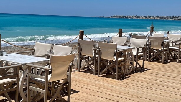 Un restaurante frente al mar con terraza de madera y mesas, con vista al océano.