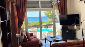Sala de estar con sofá, televisor y vista a la piscina.