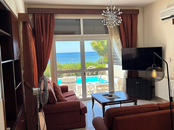 Sala de estar con sofá, televisor y vista a la piscina.