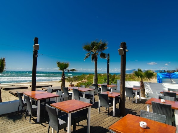 An outdoor seating area with tables and chairs, overlooking the beach and ocean.