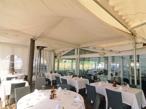 A tented dining area with round tables, chairs, and glass walls.