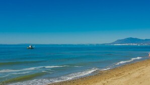 A beach with clear blue water, a boat, and a distant mountain. - 75m to Beach Luxury 4-Bed Villa with Heated Pool & Oasis Patio in Marbella (Marbella)