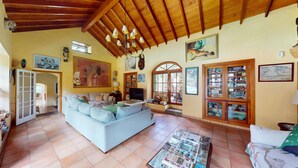 A spacious living room with a light blue sofa, wooden ceiling beams, and a large window with a view of the outdoors. - Country house with heated swimming pool for exclusive use between the sea and the mountains.  (Lomo de San Pedro)