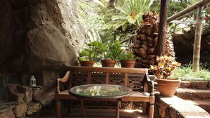 A rustic outdoor seating area with a wooden bench and a glass table, surrounded by potted plants and a stone wall. - Country house with heated swimming pool for exclusive use between the sea and the mountains.  (Lomo de San Pedro)
