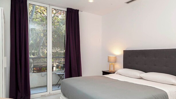 Une chambre à coucher avec un lit, une table de chevet avec une lampe, et une vue sur l’extérieur grâce à une porte coulissante.