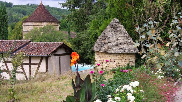 A rustic stone building with a conical roof, surrounded by lush greenery and flowering plants. - Charming holiday cottage in the heart of the Périgord Noir (Plazac)
