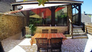 A covered outdoor seating area with a table and chairs, stone walls, and a view of the surrounding buildings. - Charming holiday cottage in the heart of the Périgord Noir (Plazac)