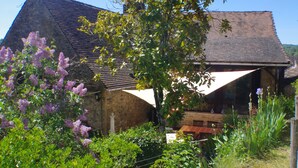 A rustic stone building with a sloped roof, surrounded by lush greenery and flowering plants. - Charming holiday cottage in the heart of the Périgord Noir (Plazac)
