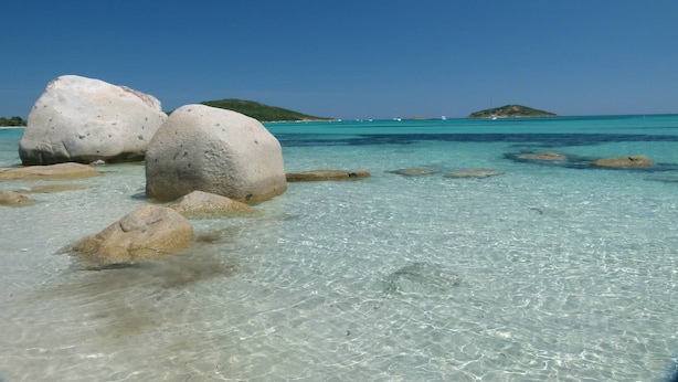 Una playa despejada con rocas grandes y aguas turquesas tranquilas.