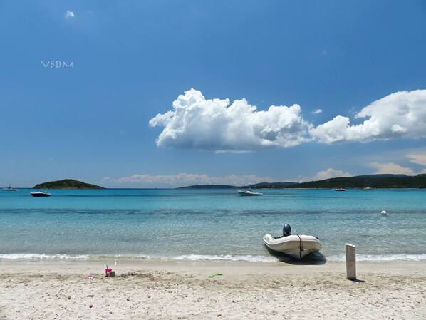 A beach with a boat on the shore, calm water, and distant boats. - Sea View Villa 180 - Heated pool - Beaches 2 min - 5 bedrooms - Wifi Clim (Zonza)
