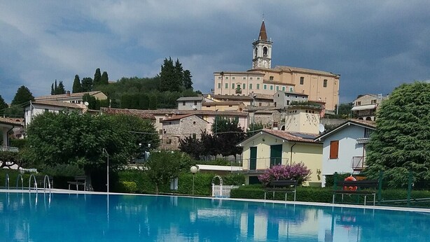 A swimming pool with clear blue water, surrounded by buildings and trees. - Villetta Gelsomino, in Bardolino Calmasino villa in residence with swimming pools. (Calmasino)