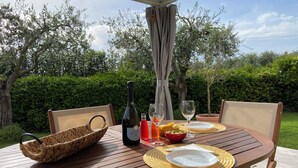 A wooden table set outdoors with a bottle of wine, glasses, a basket, and a plate. - Villetta Gelsomino, in Bardolino Calmasino villa in residence with swimming pools. (Calmasino)
