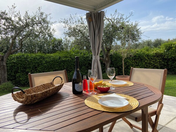 Una mesa de madera al aire libre con una botella de vino, copas, una cesta y un plato.