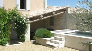 Un edificio de piedra con techo de tejas, un pequeño jardín con grava y una fuente de agua.