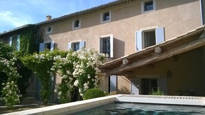 Un edificio con piscina, terraza cubierta y arbustos florecientes de color blanco.