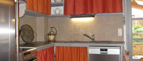 A compact kitchen with a dishwasher, oven, and a small dining area with chairs.