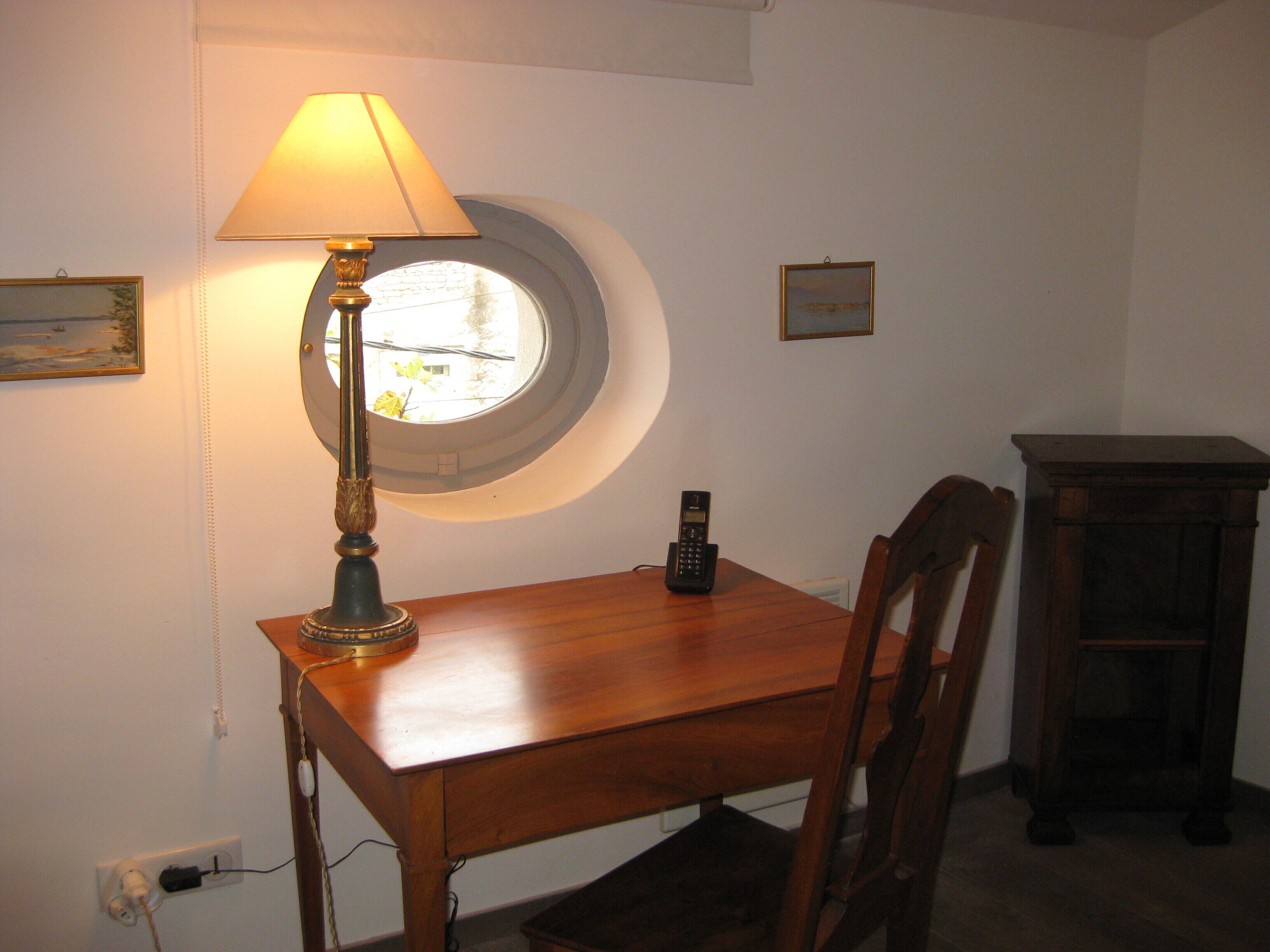 Une pièce avec une table en bois, une lampe, un téléphone et une petite fenêtre.