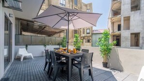 A patio with a table set for two, surrounded by chairs, a large umbrella, and potted plants.