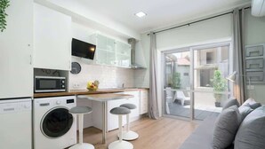 A compact kitchen with a washing machine, a microwave, and a dining area with stools.