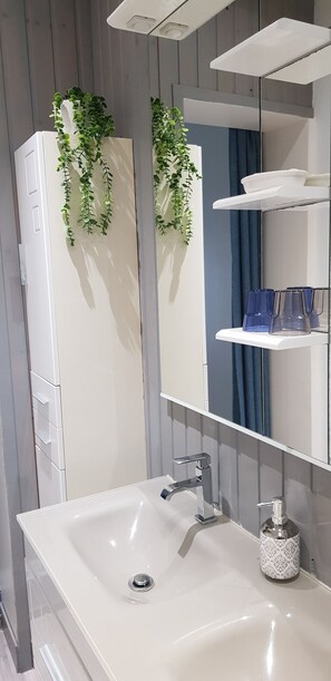 Ett modernt badrum med en vit tvättställ, en spegel och en hylla med blå glas.