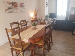 A dining area with a wooden table and chairs, a potted plant, and a painting on the wall.