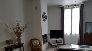 Ett vardagsrum med en tv, en soffa, en fåtölj, ett litet bord med en vas och en väggklocka.