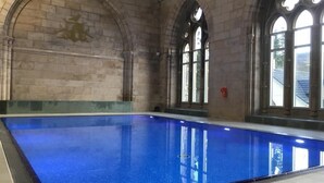 Una piscina interior con paredes de piedra y ventanas arqueadas.