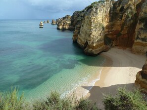 A coastal landscape with clear turquoise waters, sandy beach, and rocky cliffs.