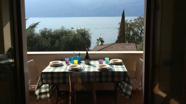 A table set for two with a checkered tablecloth, plates, cups, and a bottle, overlooking a body of water with a mountain in the background.
