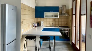 A modern kitchen with a white refrigerator, blue cabinets, a white countertop, and two black bar stools.