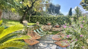 A patio with wicker chairs, a stone wall, and various potted plants.