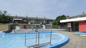 Una piscina con borde azul, barandales metálicos y un muro de ladrillo al fondo.