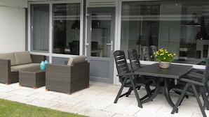 Un patio al aire libre con mesa de comedor, sillas, un sofá y una mesa pequeña con un cesto de flores.