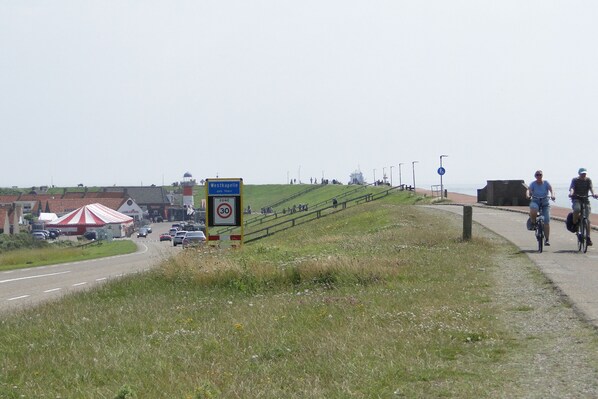 A coastal road with a speed limit sign, a pedestrian path, and a beach area with people and a red and white tent.