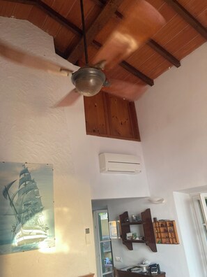 A room with a ceiling fan, an air conditioning unit, a wooden ceiling, a wall-mounted shelf with items, and a door leading to another room. - House / Villa - Elba (Portoferraio)