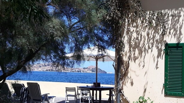 Una terrazza con posti a sedere all'aperto, vista sul mare e un edificio con persiana verde.