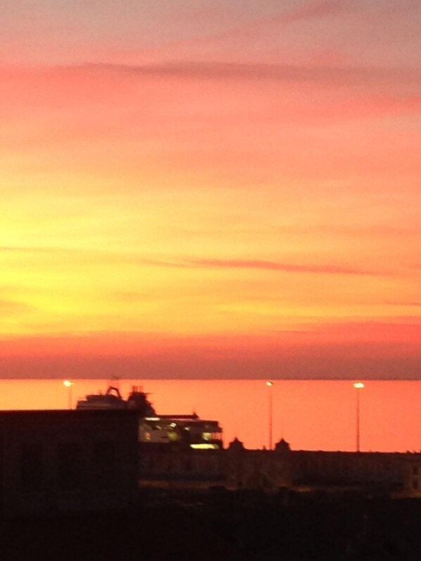 A sunset over a body of water with buildings silhouetted against the sky. - Penthouse in the center with sea view (Trieste)