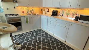 Une cuisine moderne avec des meubles blancs, un tapis noir à motifs, une cuisinière à gaz, un four à micro-ondes et une machine à café.