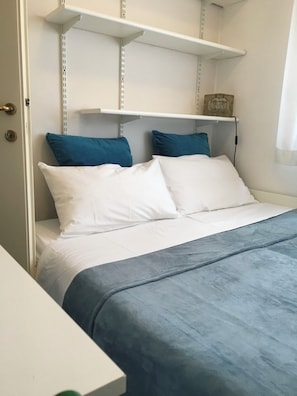 Una cama con ropa de cama blanca y azul, un cabecero blanco y una repisa sobre la cama.