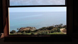 A view through a window of a coastal landscape with a clear sky, calm sea, and rocky terrain. - House "The two Lapwing" (semi-detached portion) (Marina di Tertenia, Tertenia (OG))