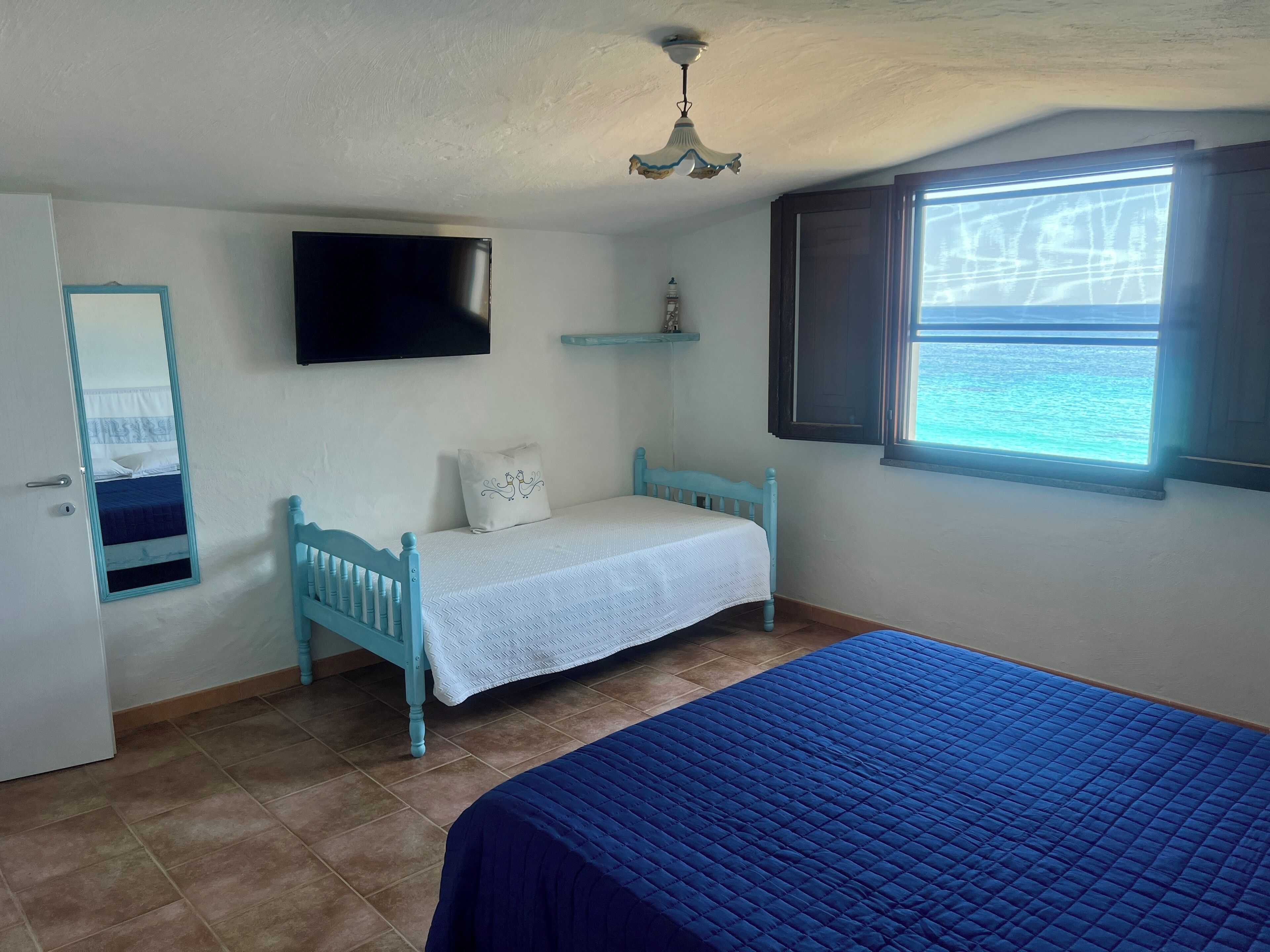 A bedroom with a bed, a TV, a window with a view, and a ceiling fan.