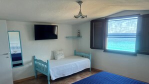 A bedroom with a bed, a TV, a window with a view, and a ceiling fan. - House "The two Lapwing" (semi-detached portion) (Marina di Tertenia, Tertenia (OG))