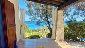 A terrace with a table set for a meal, a bottle, and a glass of wine, overlooking a scenic view of the sea and greenery. - House "The two Lapwing" (semi-detached portion) (Marina di Tertenia, Tertenia (OG))