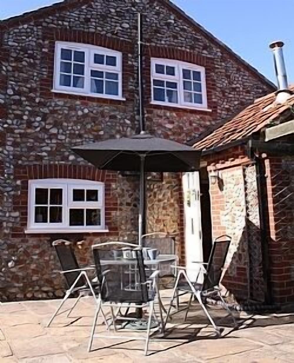 A stone building with a tiled roof, a chimney, and a patio with a table and chairs.
