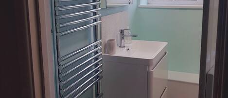 A bathroom with a glass shower enclosure, a white sink, and a window with frosted glass.