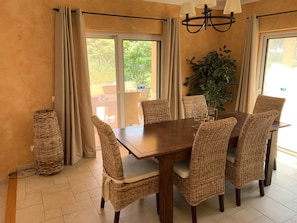 A dining area with a wooden table and wicker chairs, a potted plant, and a chandelier.