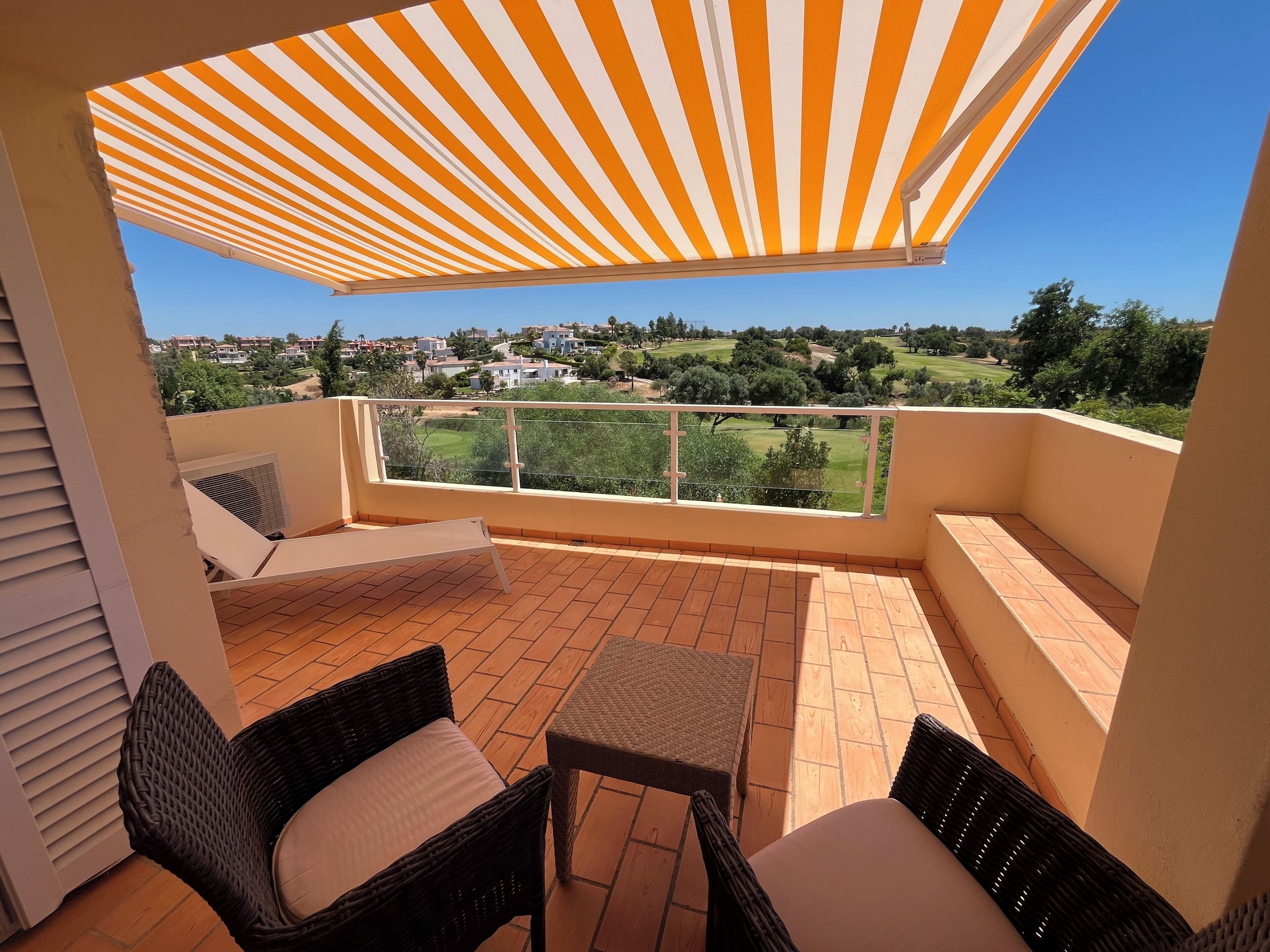 A balcony with a striped awning, wicker furniture, and a view of a residential area.