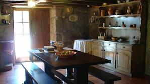 A rustic kitchen with wooden cabinets, a stone wall, and a wooden table with a bowl of fruit. - Cete: house / villa - Cête (Cête)